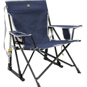 Person enjoying a relaxing moment in the GCI Outdoor Kickback Rocker Chair by a campfire, showcasing the chair's portability and comfort